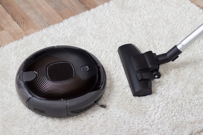 Traditional vacuum cleaner with a hose, nozzle and brush versus a modern circular automated low profile unit, high angle view on a shaggy white carpet