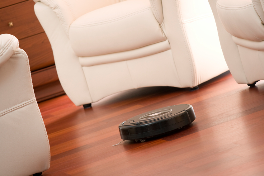 Home vacuum cleaning robot in action on genuine wooden floor. Selective focus on robot.