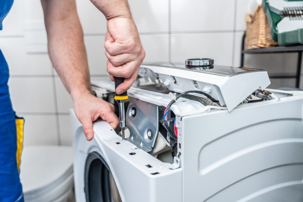 Repairman using a screwdriver disassembles a washing machine for repair - AHAM Consumer Blog
